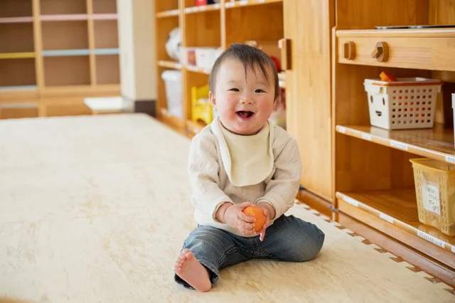 おもちゃのみかんを持って笑顔でお座りする赤ちゃん