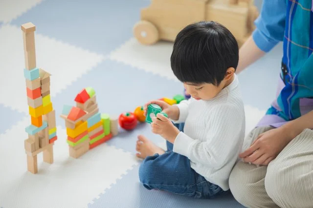積み木やおもちゃで遊ぶ男の子と見守る大人